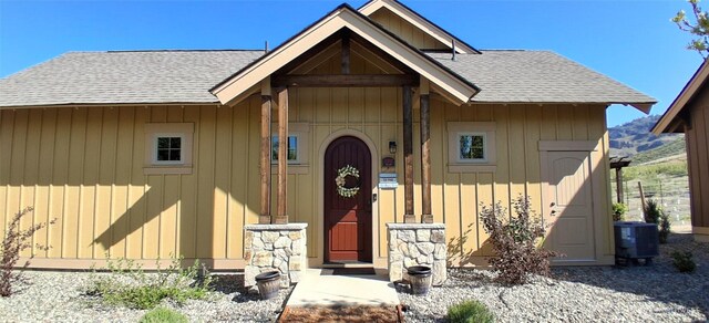 view of front of house with board and batten siding, roof with shingles, and central AC
