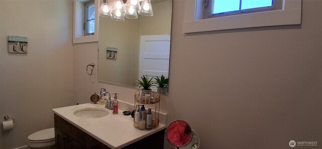 half bath featuring vanity, plenty of natural light, toilet, and a chandelier
