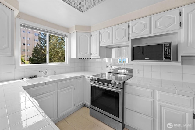 kitchen with appliances with stainless steel finishes, tile counters, a sink, and white cabinets