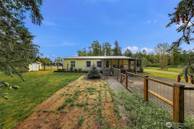 back of house featuring a lawn, fence, an outdoor structure, and metal roof