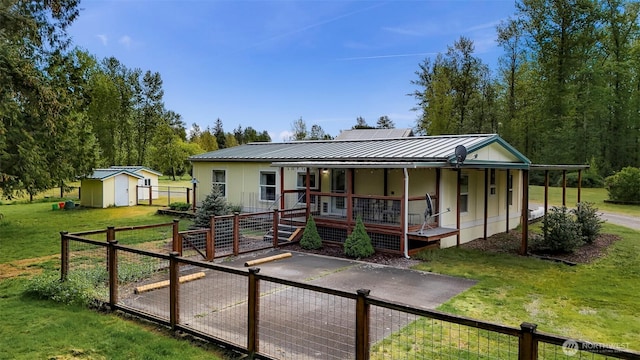 back of house featuring covered porch, an outbuilding, metal roof, a lawn, and a storage shed
