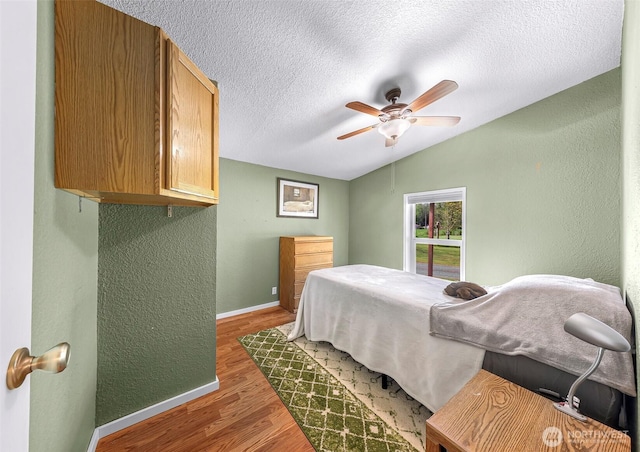 bedroom featuring a textured ceiling, vaulted ceiling, baseboards, light wood finished floors, and a textured wall