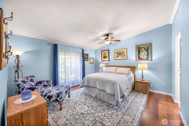 bedroom with wood finished floors, lofted ceiling, baseboards, a textured ceiling, and a ceiling fan