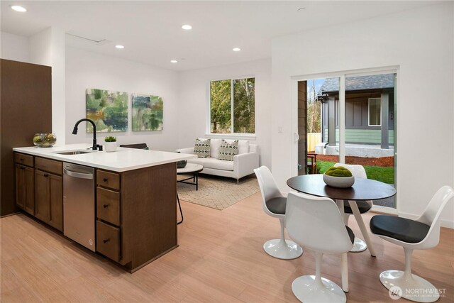 kitchen with a sink, light countertops, stainless steel dishwasher, and light wood-style flooring