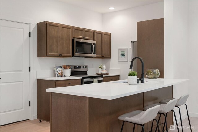 kitchen featuring a kitchen breakfast bar, light countertops, a sink, light wood-style flooring, and stainless steel appliances
