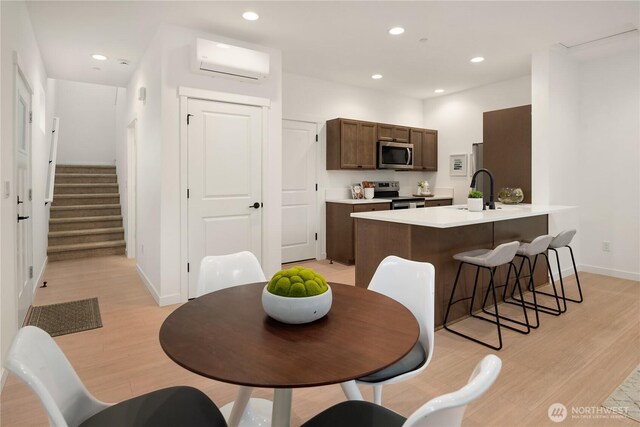 kitchen featuring stainless steel appliances, a sink, a wall unit AC, and light wood-style flooring