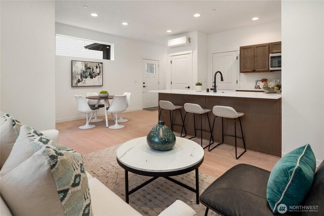 living area with recessed lighting, baseboards, a wall unit AC, and light wood finished floors