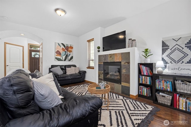 living area featuring baseboards, arched walkways, wood finished floors, and a tile fireplace