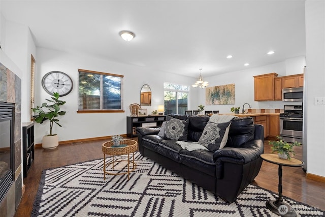 living area with an inviting chandelier, a tiled fireplace, recessed lighting, baseboards, and wood finished floors