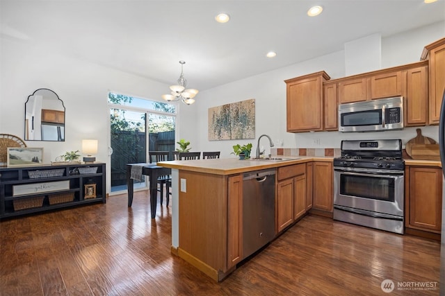 kitchen featuring a peninsula, a chandelier, a sink, dark wood finished floors, and appliances with stainless steel finishes