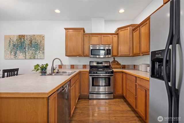 kitchen with a sink, light countertops, stainless steel appliances, a peninsula, and dark wood-style floors
