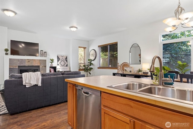 kitchen with a tile fireplace, a sink, dark wood finished floors, dishwasher, and a notable chandelier