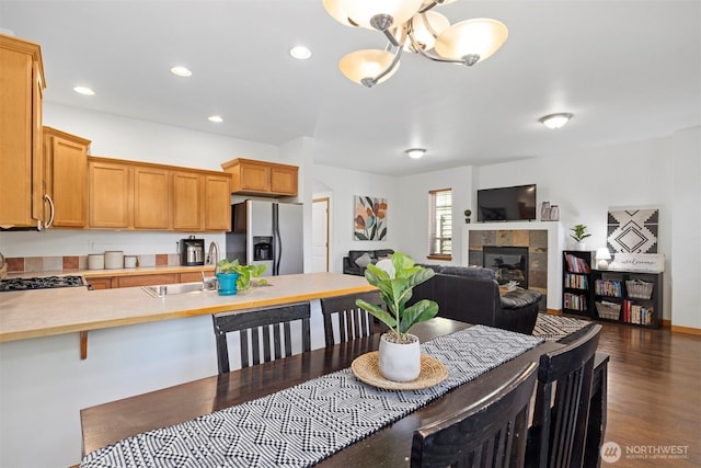 dining space featuring a tiled fireplace, recessed lighting, dark wood-style floors, and a chandelier