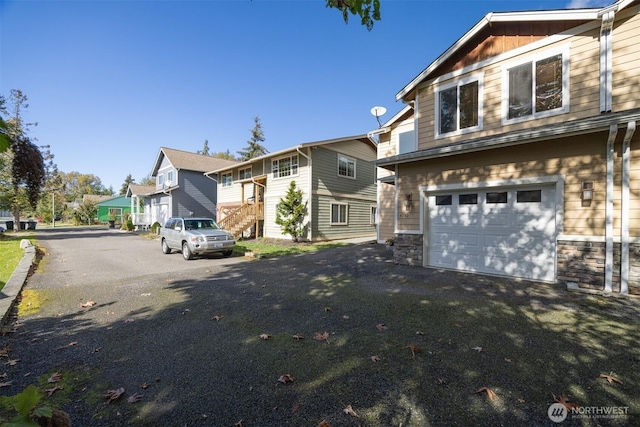 view of front facade featuring a residential view, aphalt driveway, an attached garage, stairs, and stone siding