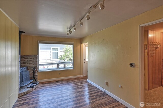 unfurnished living room featuring a wood stove, rail lighting, wood finished floors, and baseboards