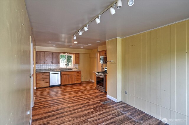 kitchen featuring stainless steel appliances, a sink, dark wood-type flooring, rail lighting, and backsplash