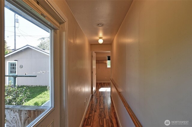 hallway with dark wood-type flooring, baseboards, and an upstairs landing