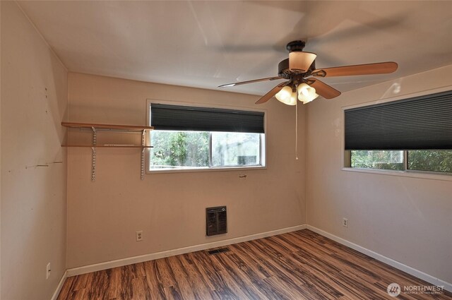 empty room with healthy amount of natural light, wood finished floors, a ceiling fan, and baseboards
