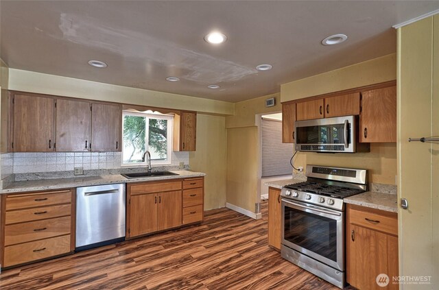 kitchen with stainless steel appliances, a sink, dark wood finished floors, light countertops, and decorative backsplash