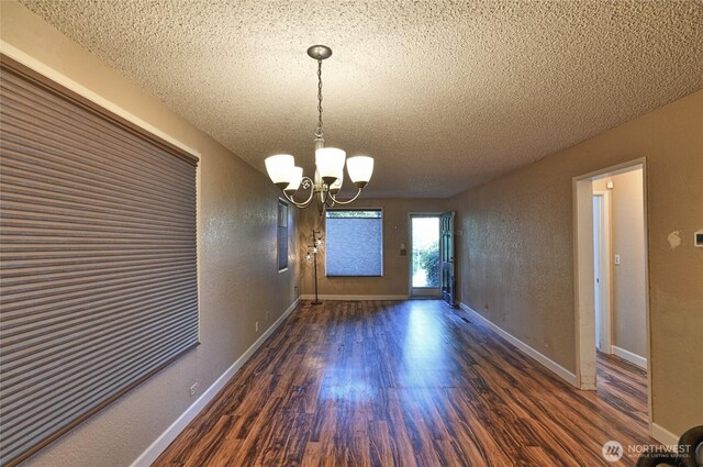 unfurnished dining area with a textured ceiling, wood finished floors, a chandelier, and baseboards