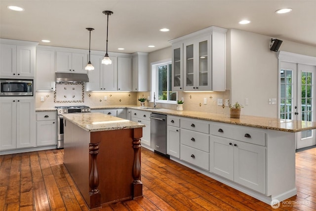 kitchen featuring under cabinet range hood, stainless steel appliances, a healthy amount of sunlight, and a peninsula