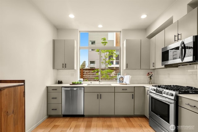 kitchen with gray cabinets, appliances with stainless steel finishes, tasteful backsplash, a sink, and light countertops