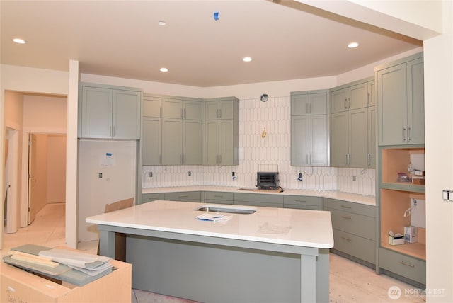 kitchen with light countertops, recessed lighting, a toaster, backsplash, and a center island with sink