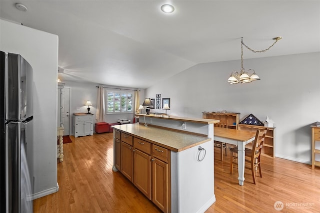 kitchen featuring freestanding refrigerator, pendant lighting, lofted ceiling, a kitchen island, and light wood-type flooring