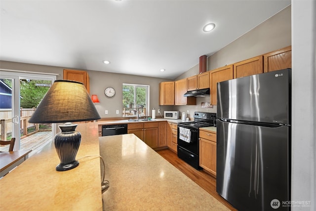 kitchen with a sink, light countertops, wood finished floors, under cabinet range hood, and black appliances