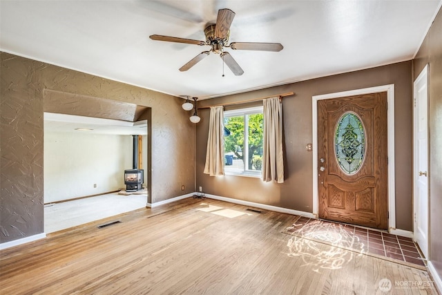 entrance foyer with visible vents, a wood stove, wood finished floors, baseboards, and a ceiling fan