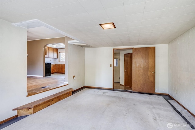 carpeted spare room featuring arched walkways and baseboards