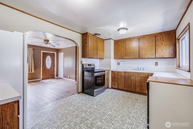 kitchen with stainless steel electric range oven, a sink, light countertops, arched walkways, and brown cabinetry