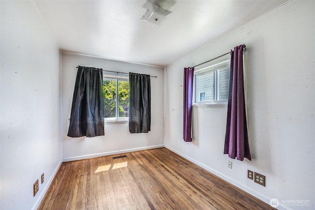 spare room with baseboards, visible vents, and wood finished floors