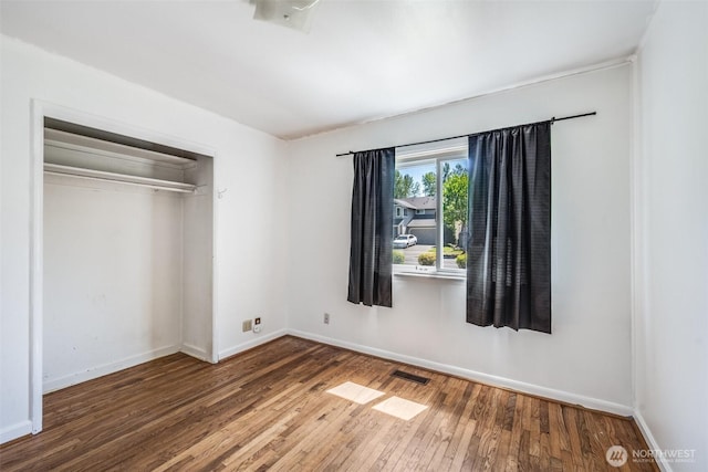 unfurnished bedroom with baseboards, visible vents, wood finished floors, and a closet