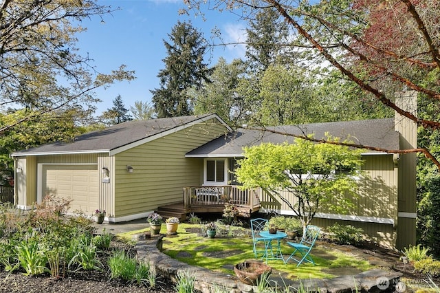 rear view of property featuring a wooden deck, a shingled roof, and a garage
