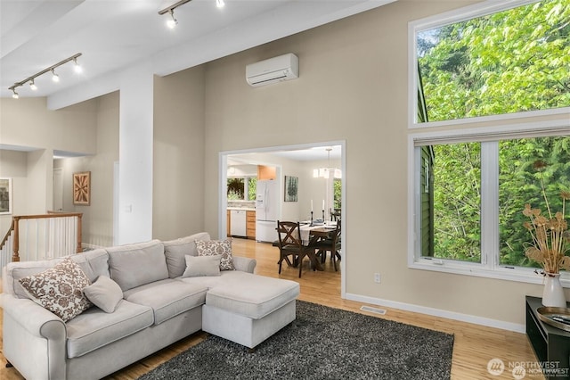 living area with track lighting, visible vents, a towering ceiling, wood finished floors, and a wall unit AC