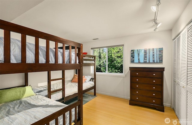 bedroom featuring light wood-style floors, baseboards, visible vents, and a closet