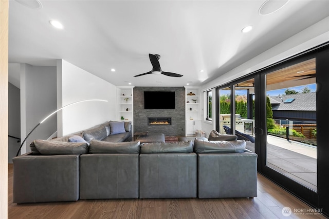 living room featuring wood finished floors, a fireplace, ceiling fan, recessed lighting, and built in shelves