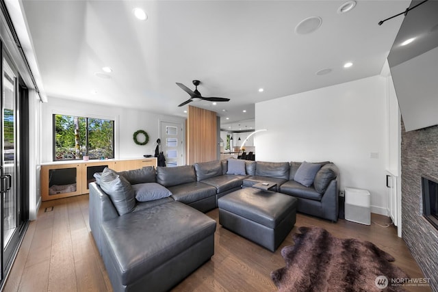 living room featuring recessed lighting, ceiling fan, a stone fireplace, and wood finished floors