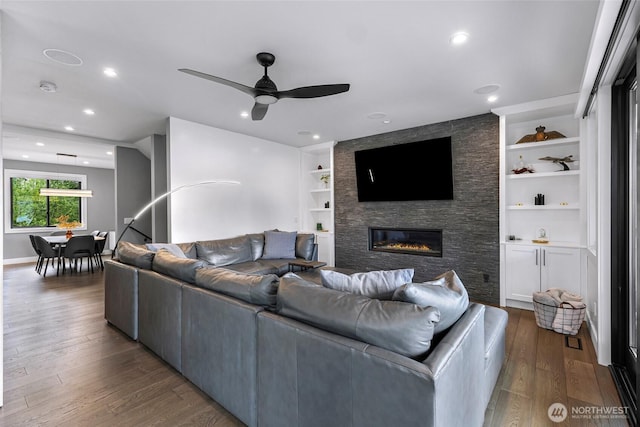 living area with a ceiling fan, built in features, a fireplace, wood finished floors, and recessed lighting