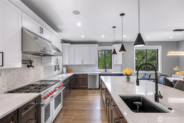 kitchen with white cabinets, hanging light fixtures, appliances with stainless steel finishes, a sink, and under cabinet range hood