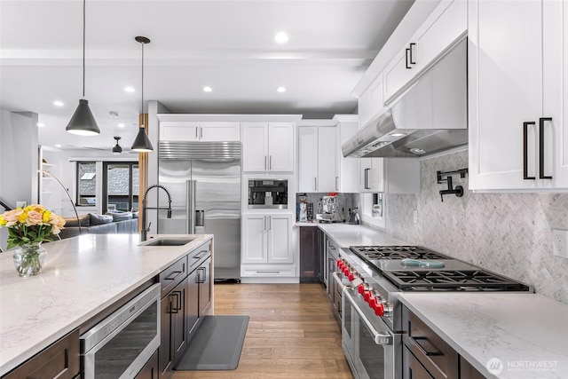 kitchen with built in appliances, white cabinets, under cabinet range hood, and decorative light fixtures