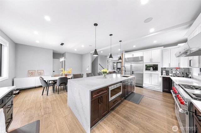 kitchen featuring a center island with sink, a sink, light wood-style floors, built in appliances, and white cabinetry
