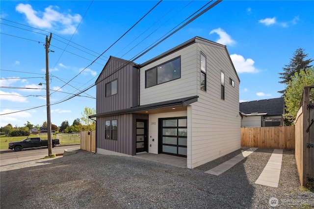 contemporary house featuring board and batten siding, an attached garage, fence, and driveway