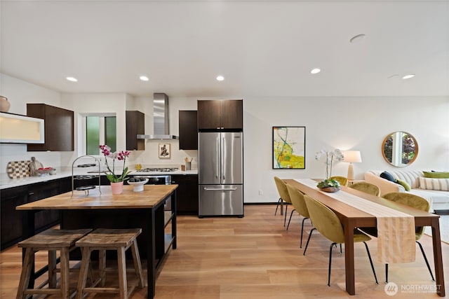 kitchen with butcher block countertops, light wood-type flooring, recessed lighting, wall chimney exhaust hood, and stainless steel appliances