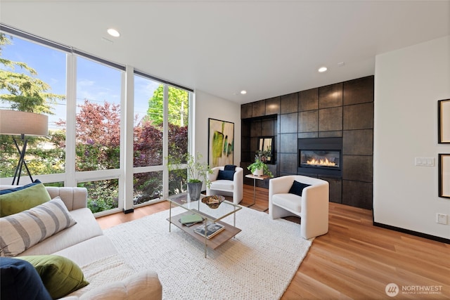 living room with a wall of windows, recessed lighting, baseboards, light wood-type flooring, and a tile fireplace