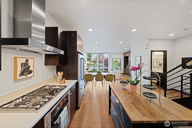 kitchen featuring wall chimney range hood, appliances with stainless steel finishes, modern cabinets, light wood-style flooring, and butcher block counters