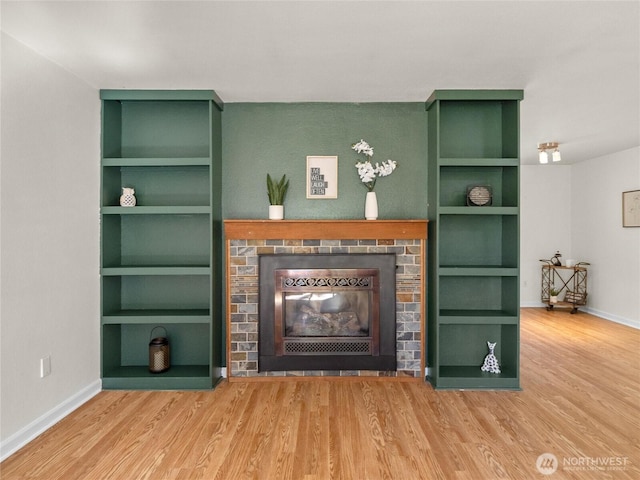 living area featuring a brick fireplace, baseboards, built in shelves, and wood finished floors
