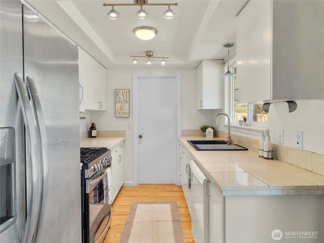 kitchen featuring light wood-type flooring, a raised ceiling, white cabinets, a sink, and stainless steel appliances