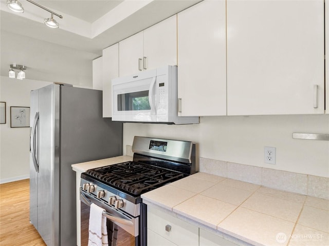 kitchen with white cabinets, appliances with stainless steel finishes, light wood finished floors, light countertops, and rail lighting